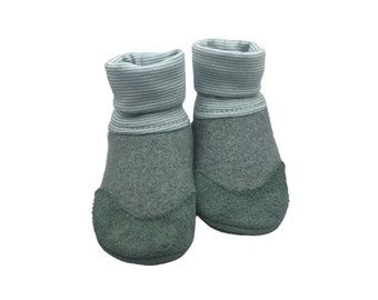 Puede incluir: Un par de botines grises para bebé con suela de ante verde y un puño a rayas azul claro.