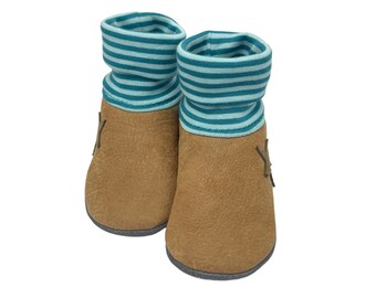 Puede incluir: Un par de botitas de bebé de cuero marrón con puños a rayas azul verdoso y blanco.