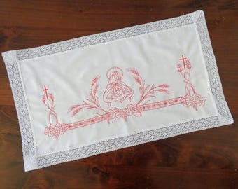 Könnte beinhalten: Ein weißer Leinen-Altartuch mit einem roten gestickten Design der Jungfrau Maria und des Jesuskindes, umgeben von Weizenähren und Kreuzen.