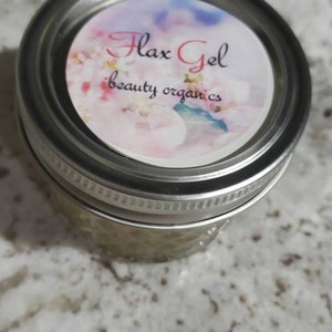 May include: A clear glass jar with a silver lid. The lid has a white label with pink and blue watercolor flowers and the text "Flax Gel beauty organics".