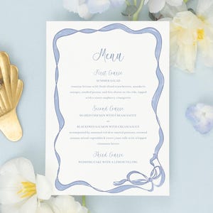 May include: A blue and white wedding menu card with a decorative border and a blue ribbon. The menu includes a summer salad, seared salmon with cream sauce, and wedding cake with lemon filling.