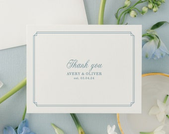 May include: A white thank you card with a blue border and the text "Thank you Avery & Oliver est. 03.04.24". The card is surrounded by white and pink flowers on a light blue background.