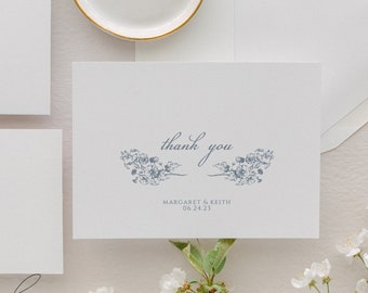 May include: A white thank you card with blue floral accents and the text "thank you" in cursive. Below the floral accents is the text "Margaret & Keith 06.24.23".