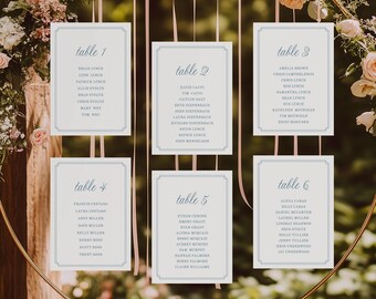 Pode incluir: Um aro de metal dourado decorado com flores e folhagens, segurando seis cartões brancos com bordas azuis. Cada cartão exibe os nomes dos convidados e os números das mesas. Fitas cor-de-rosa pendem do aro, ideal para um casamento.