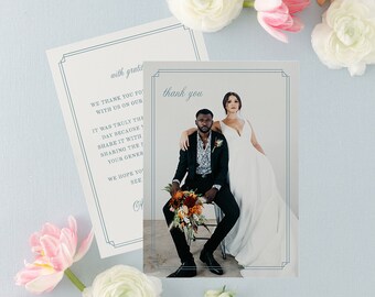 May include: A wedding thank you card with a photo of a bride and groom. The card has a blue border and the text "thank you" in a script font. The photo shows the bride and groom standing together, the bride is wearing a white dress and the groom is wearing a black suit. The card is surrounded by flowers.
