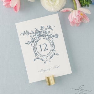 May include: A white card with a blue floral design and the number 12 in a circle. The text "Margaret & Heath" is written in cursive at the bottom of the card.