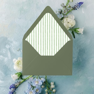 May include: An open olive green envelope with a light green and white striped interior, set against a light blue backdrop with white and blue flowers. The envelope's interior features a vertical stripe design.