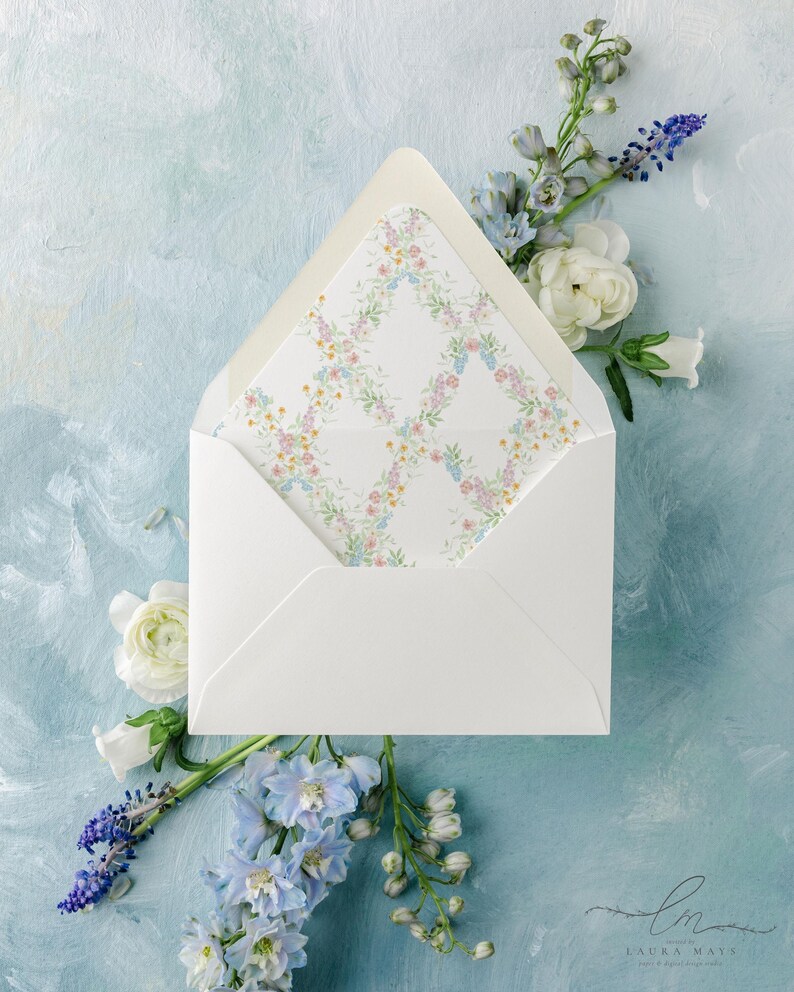 May include: A white envelope with a floral patterned liner, open to reveal the design. The liner features a delicate pattern of pink, yellow, and blue flowers. The envelope is surrounded by white and blue flowers on a light blue painted background.