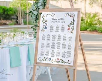 May include: A wooden easel displays a seating chart for a wedding. The white sign has floral accents and the names of the guests. The text reads "Allison and Paul, we saved you a seat". The table setting includes white linens and mint green napkins.