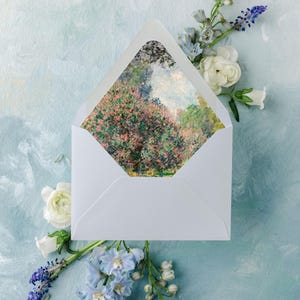 May include: A white envelope displaying a landscape painting, set against a light blue backdrop with white and blue flowers. The painting shows pink and green foliage. The image has a still life composition, with a soft, artistic style.