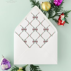 May include: A white envelope with a patterned interior featuring a grid of red bows and green garland. The envelope is surrounded by Christmas ornaments and greenery, including a purple house, a gold ball, and a red Santa.