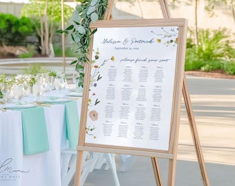 May include: A wooden easel displaying a wedding seating chart. The chart features the names "Melissa & Patrick" and the date "September 14, 2024." Floral accents and a "please find your seat" message adorn the top. Tables are listed below.