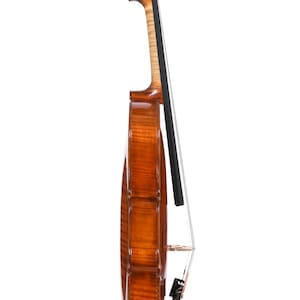 Puede incluir: Vista lateral de un viol&iacute;n con un acabado marr&oacute;n brillante. El instrumento presenta un clavijero en espiral, un m&aacute;stil de color claro y un diapas&oacute;n negro. Las cuerdas son visibles, y el puente y el cordal est&aacute;n en su lugar. El viol&iacute;n est&aacute; sobre un fondo blanco.