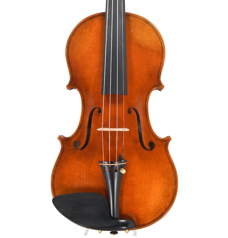 Puede incluir: Primer plano de un viol&iacute;n con un acabado marr&oacute;n c&aacute;lido. El instrumento presenta un diapas&oacute;n negro, cuerdas y mentonera. Se ven las efes y el rollo, sobre un fondo blanco.