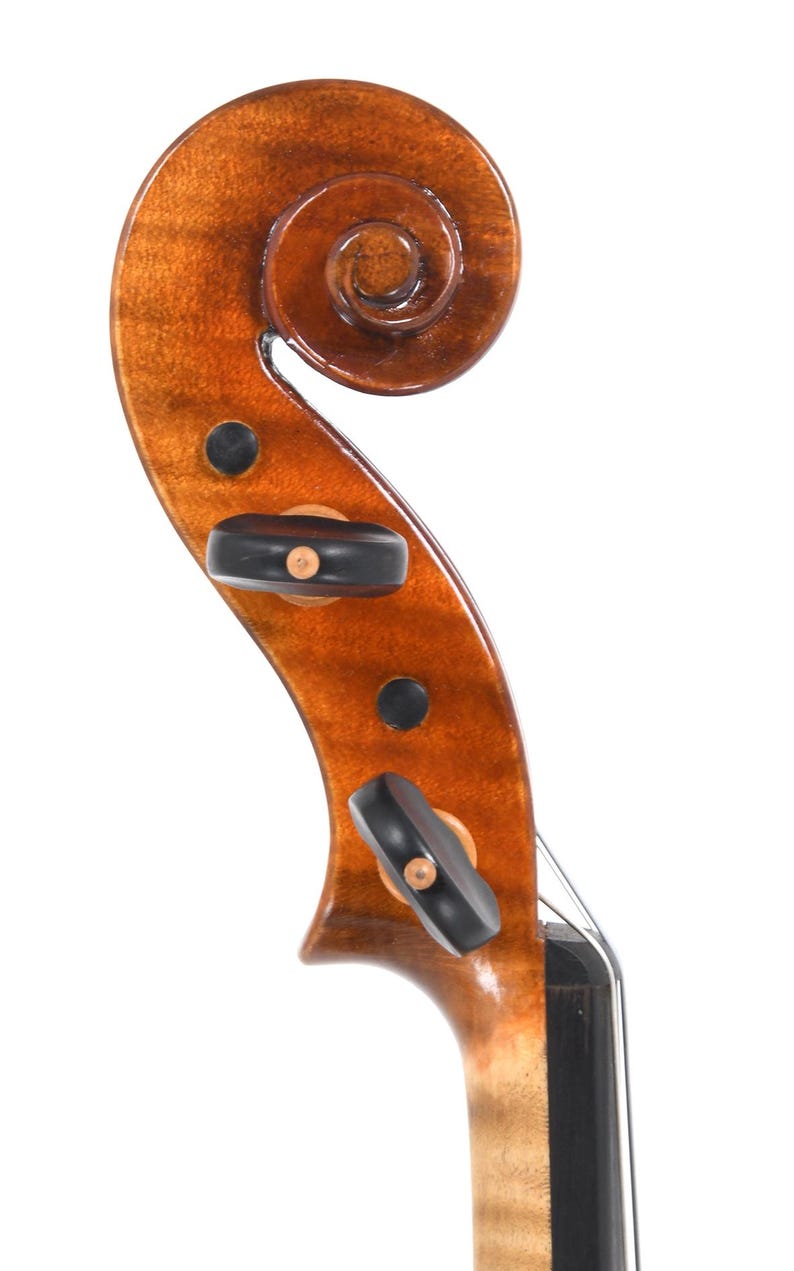 Puede incluir: Primer plano del clavijero y el voluta de un viol&iacute;n. La madera tiene un tono marr&oacute;n rojizo c&aacute;lido con un acabado brillante. El voluta es una espiral apretada y elegante. Se ven clavijas negras, junto con peque&ntilde;as incrustaciones circulares oscuras.