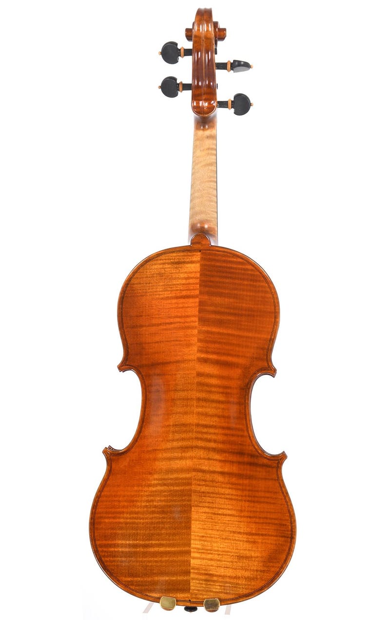 Puede incluir: Vista trasera de un viol&iacute;n, mostrando su construcci&oacute;n de madera. El viol&iacute;n tiene un acabado marr&oacute;n &aacute;mbar c&aacute;lido con vetas de madera visibles. El m&aacute;stil y el clavijero tambi&eacute;n son visibles, con clavijas de afinaci&oacute;n en la parte superior. El instrumento est&aacute; sobre un fondo blanco.