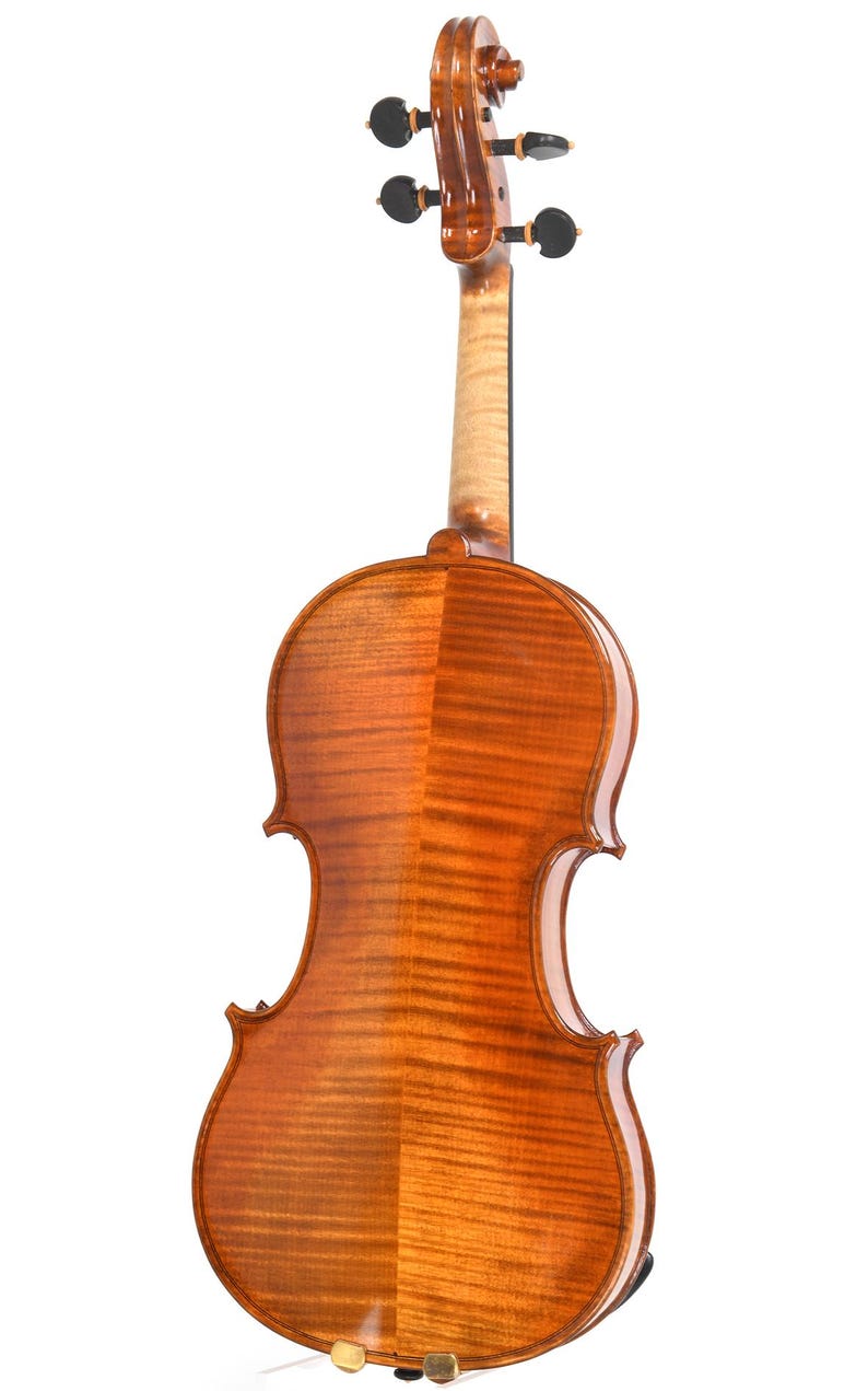 Puede incluir: Primer plano de la parte trasera de un viol&iacute;n, que muestra la veta de la madera en tonos &aacute;mbar c&aacute;lidos. La forma del instrumento es visible, con sus bordes curvos y el m&aacute;stil que se extiende hacia arriba. Tambi&eacute;n se ven las clavijas y el rollo del viol&iacute;n.