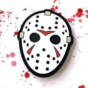 May include: A white hockey mask with black eye holes and a red slash across the forehead. The mask has a black border and is surrounded by red splatter paint.
