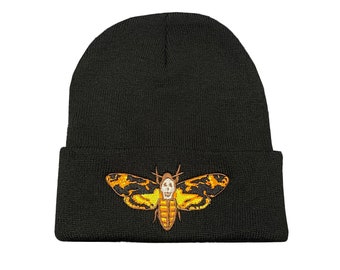 May include: Black beanie hat with an embroidered Death's-head Hawkmoth design. The moth features yellow and gold wings with a skull-like marking. The hat is made of a knitted material.