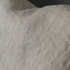 May include: Close-up of a light brown linen fabric with a textured weave. The fabric is soft and has a natural, rustic look.