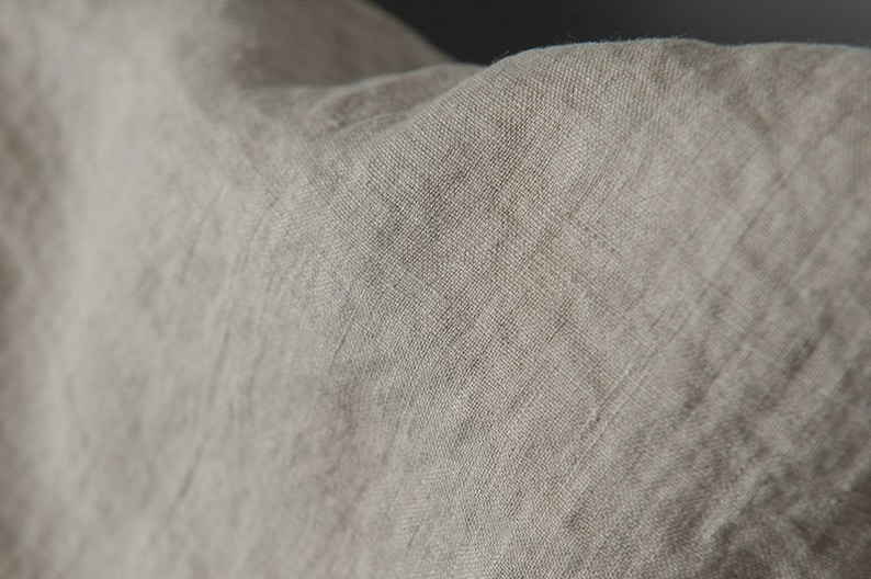 May include: Close-up of a light brown linen fabric with a textured weave. The fabric is soft and has a natural, rustic look.