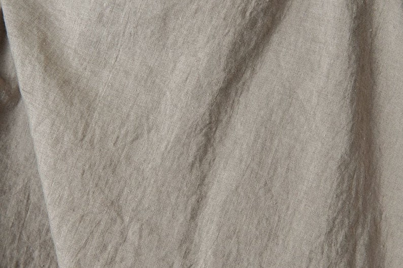May include: Close-up of a textured, light gray fabric with a subtle sheen. The fabric is wrinkled and folded, creating a soft, organic look.