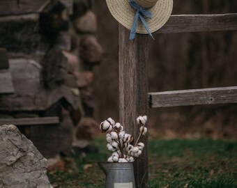 Hat and cotton stems under a cottage fence post