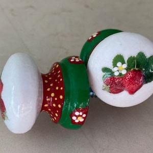 May include: Two ceramic drawer knobs with a green, red and white painted design. The knobs feature a strawberry design with white flowers.