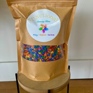 May include: A brown paper bag with a white circle label that says "Functional Sensory Bins" and "Play. Explore. Develop." The bag contains colorful plastic letters.