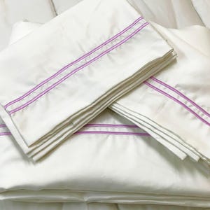 May include: A stack of white pillowcases with a double pink stripe border.