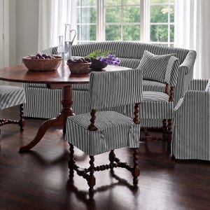 Puede incluir: Un conjunto de comedor con una mesa redonda de madera y sillas tapizadas en tela de rayas verticales blancas y negras. Las sillas tienen patas de madera torneada de color marrón oscuro. Una cesta y un cuenco con fruta oscura sobre la mesa.