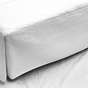 May include: White quilted bed skirt with a simple design. The skirt is made of a soft, smooth fabric and has a clean, crisp look.