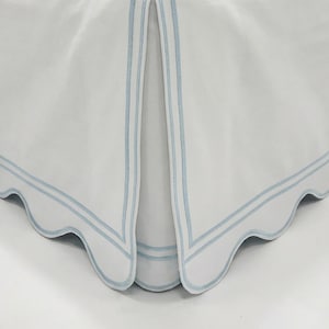 May include: White bed skirt with a scalloped edge and light blue embroidered trim. The bed skirt has a pleated design and is made of a soft, flowing fabric. The overall theme is bedding and home decor.