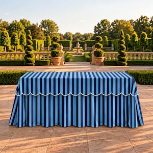 May include: A rectangular table covered with a floor-length tablecloth featuring vertical stripes in alternating shades of dark blue and light blue. The tablecloth has a scalloped edge along the top border finished with white piping.