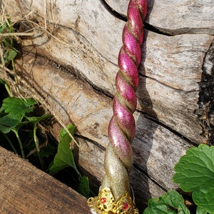 Peut inclure: Une corne de licorne en paillettes rose et or avec une couronne dorée et des bijoux rouges à la base.