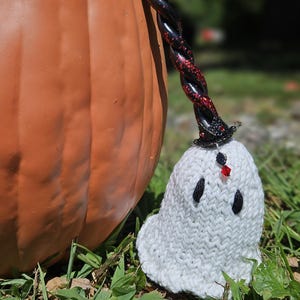 May include: A white knitted ghost with a black and red glitter witch hat sits in front of a large orange pumpkin.