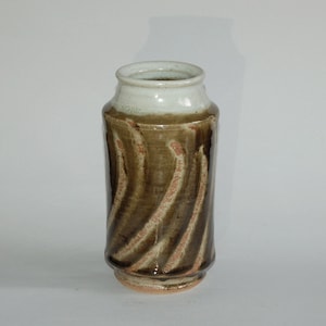 May include: A handcrafted ceramic vase with a cylindrical shape. The vase features a brown glaze with a swirling pattern and a white rim. The vase is approximately 8 inches tall.