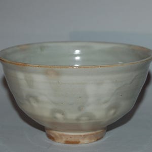 May include: A small, white ceramic bowl with a light brown glaze. The bowl has a rounded shape and a small foot.