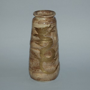 May include: A beige ceramic vase with a golden dragon design. The vase has a cylindrical shape with a slightly flared top. The dragon is intricately detailed, wrapping around the vase's body.
