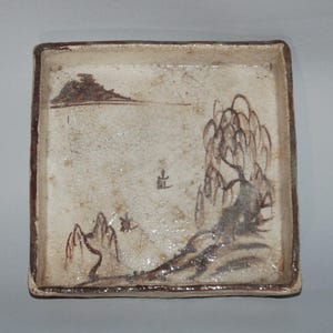 May include: A square ceramic tray with a cream-coloured glazed surface featuring a hand-painted brown landscape design. The illustration depicts a weeping willow tree, distant mountains, and a small structure. The rim is outlined in a dark brown tone.