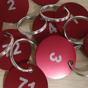 May include: A group of red key tags with silver key rings. The tags are numbered 1, 2, 3, 4, 5, 6, and 71.
