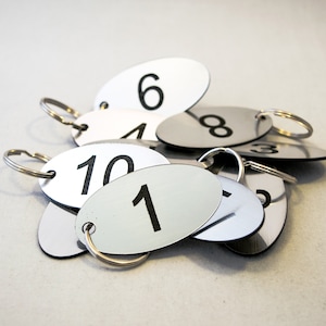 May include: A group of silver oval-shaped key tags with black numbers on them. The numbers are 1, 4, 6, 8, 10, and 3. The key tags are attached to silver key rings.