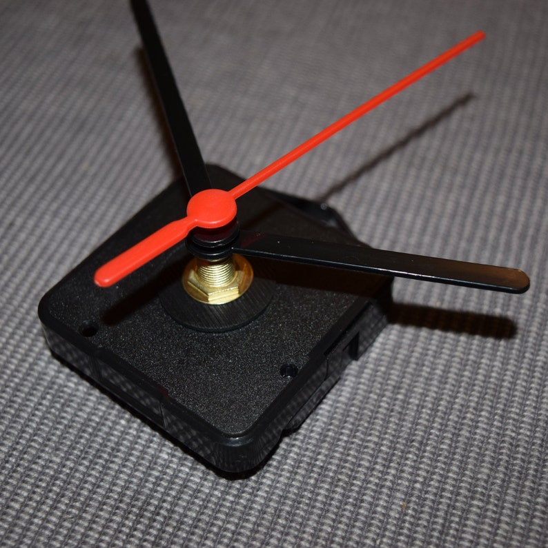 May include: A black clock mechanism with three hands. The hour hand is black, the minute hand is black, and the second hand is red.