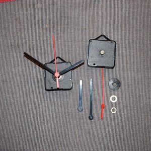May include: Two black clock mechanisms with red second hands, two black clock hands, two silver washers, and a silver nut.
