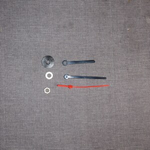 May include: Clock hands and mounting hardware. The set includes two black metal hands and one red plastic hand. There are three white plastic washers.