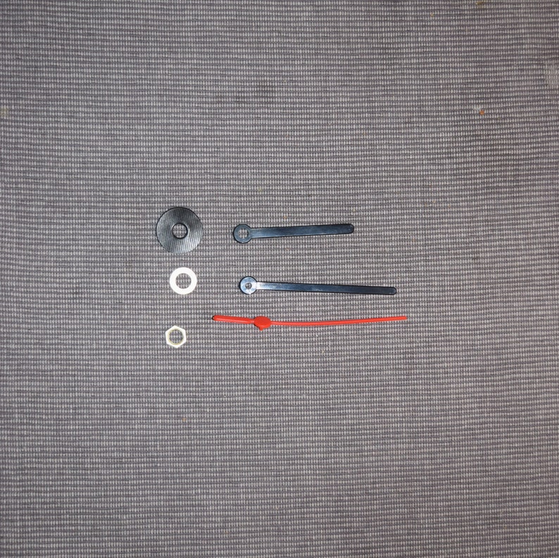 May include: Clock hands and mounting hardware. The set includes two black metal hands and one red plastic hand. There are three white plastic washers.