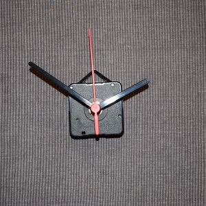 May include: A black clock mechanism with a red second hand and black hour and minute hands.