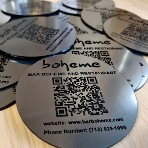 May include: Silver round coasters with a black and white QR code and the text "boheme BAR BOHEME AND RESTAURANT" and website and phone number information.