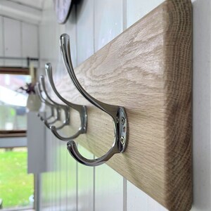 May include: A wooden coat rack with four chrome hooks. The rack is mounted on a white wall.