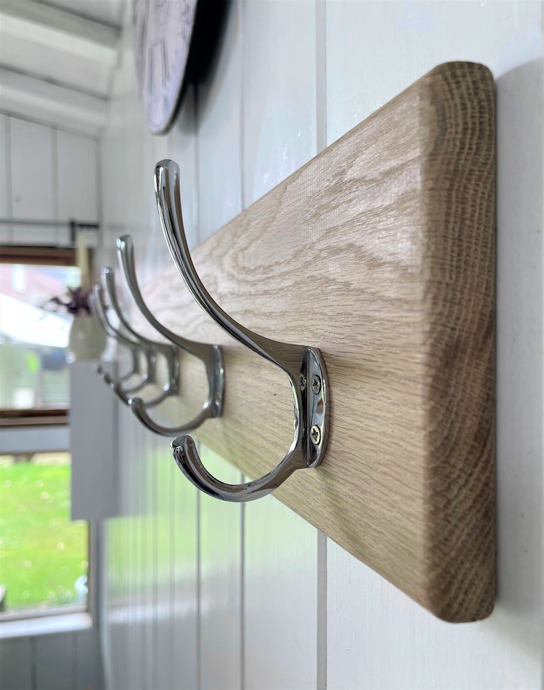 May include: A wooden coat rack with four chrome hooks. The rack is mounted on a white wall.
